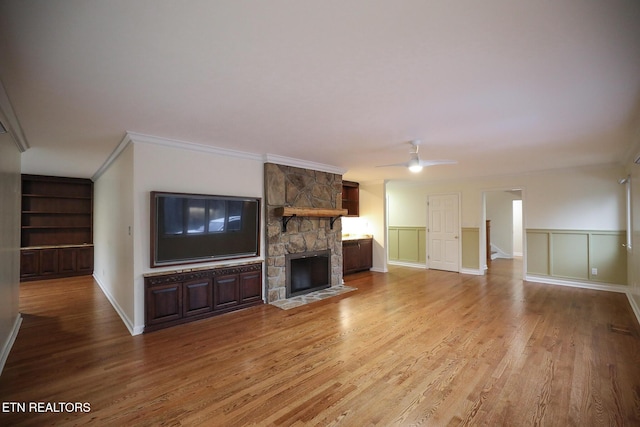 unfurnished living room featuring hardwood / wood-style flooring, crown molding, a stone fireplace, and ceiling fan