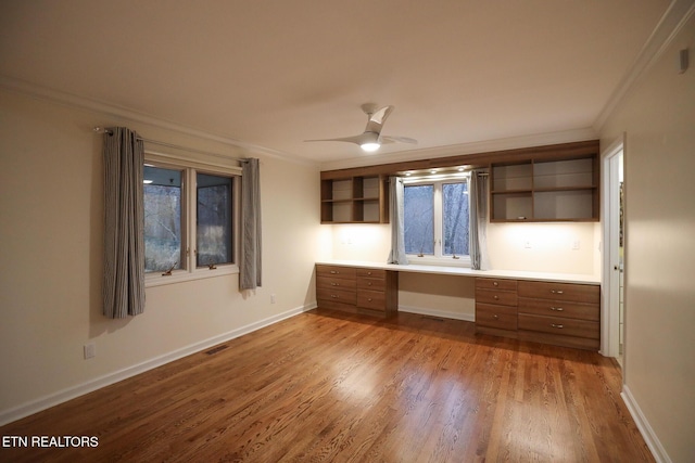 interior space with hardwood / wood-style flooring, built in desk, ornamental molding, and ceiling fan