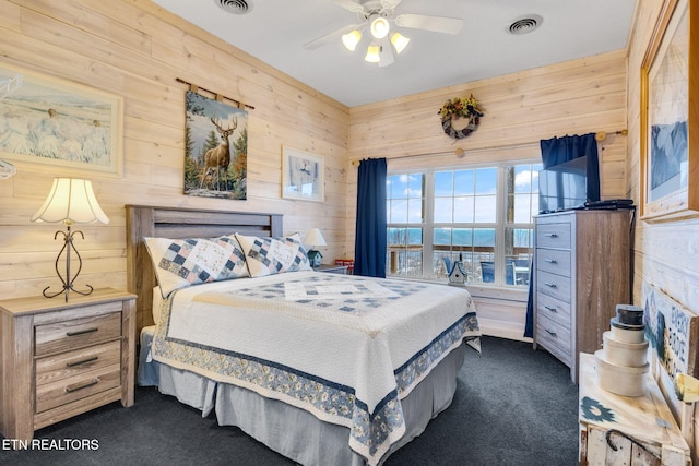 carpeted bedroom featuring ceiling fan and wood walls