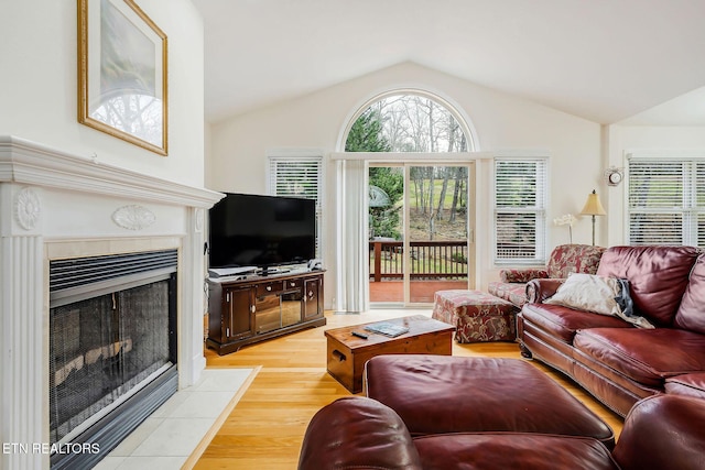 living room with a tile fireplace, vaulted ceiling, and light hardwood / wood-style flooring