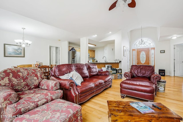 living room with sink, ceiling fan with notable chandelier, wood-type flooring, and lofted ceiling