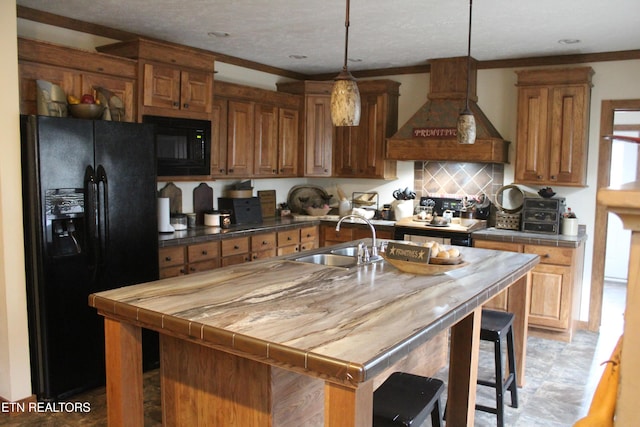 kitchen featuring a kitchen island with sink, black appliances, decorative light fixtures, and custom exhaust hood