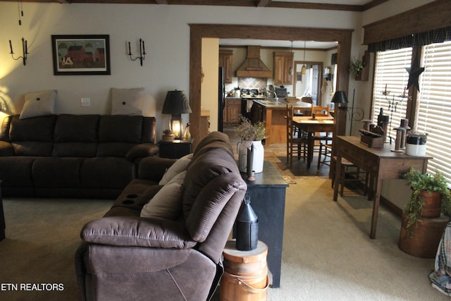 living room featuring beamed ceiling, light colored carpet, and crown molding