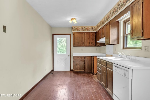 kitchen with white dishwasher, a sink, light countertops, dark wood finished floors, and under cabinet range hood
