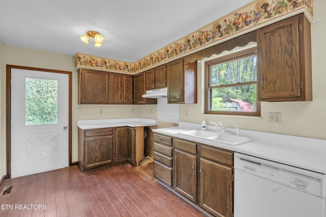 kitchen with light countertops, dishwasher, dark wood-type flooring, and a sink