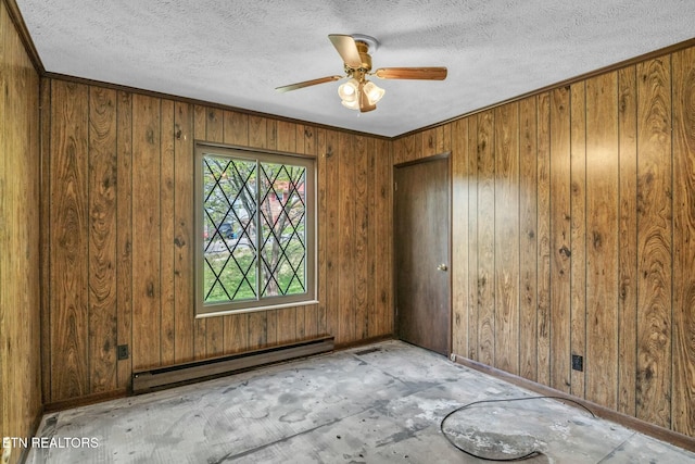 unfurnished room with a baseboard heating unit, a textured ceiling, baseboards, a ceiling fan, and wood walls