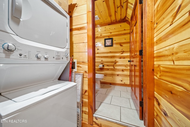 laundry area with tile patterned flooring, stacked washing maching and dryer, and wooden walls