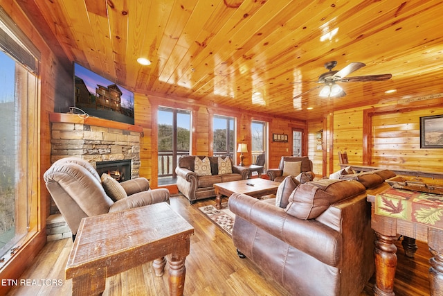 living room with a stone fireplace, wooden ceiling, wooden walls, and light hardwood / wood-style flooring