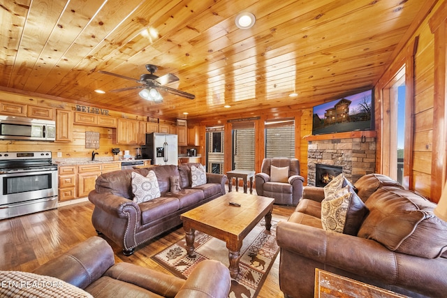 living room with ceiling fan, wooden ceiling, a fireplace, light hardwood / wood-style floors, and wood walls