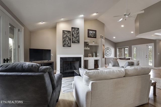 living room with ceiling fan, built in features, light wood-type flooring, and a tiled fireplace