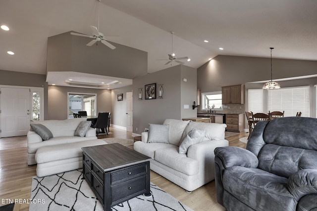 living room with ceiling fan with notable chandelier, light hardwood / wood-style floors, lofted ceiling, and sink