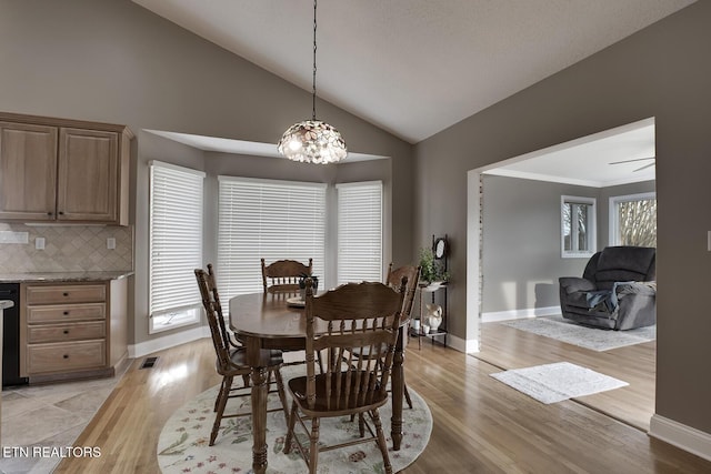 dining room featuring ceiling fan with notable chandelier, light hardwood / wood-style floors, and vaulted ceiling