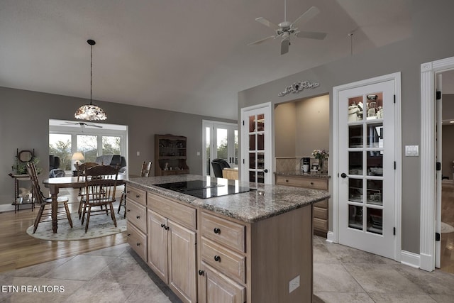 kitchen featuring black electric stovetop, decorative light fixtures, light brown cabinets, and plenty of natural light