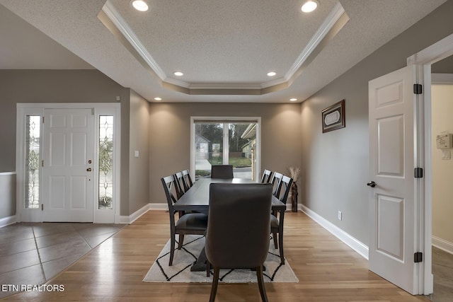 dining area featuring a textured ceiling, light wood-type flooring, ornamental molding, and a tray ceiling