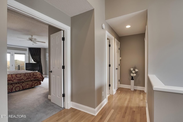 hallway with light wood-type flooring and a textured ceiling