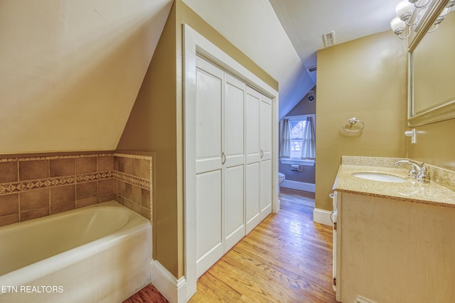 bathroom with a washtub, vanity, vaulted ceiling, hardwood / wood-style flooring, and toilet