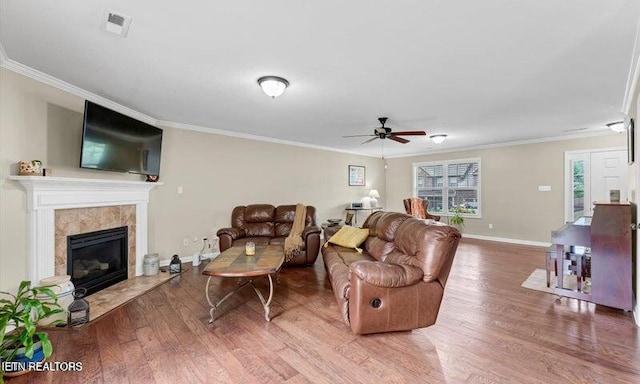 living room featuring a tile fireplace, wood-type flooring, ceiling fan, and crown molding