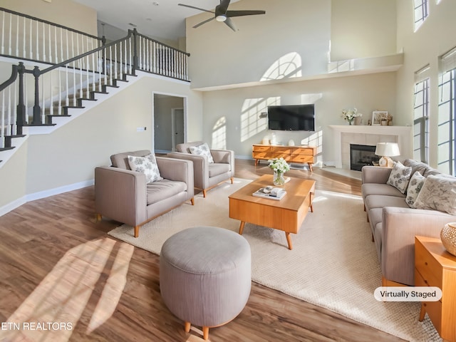 living room featuring a tile fireplace, a high ceiling, hardwood / wood-style flooring, and ceiling fan