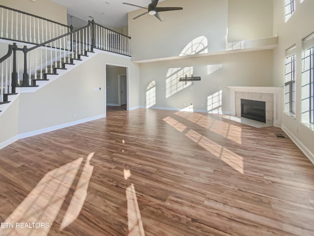 unfurnished living room with a tile fireplace, ceiling fan, a healthy amount of sunlight, and wood-type flooring