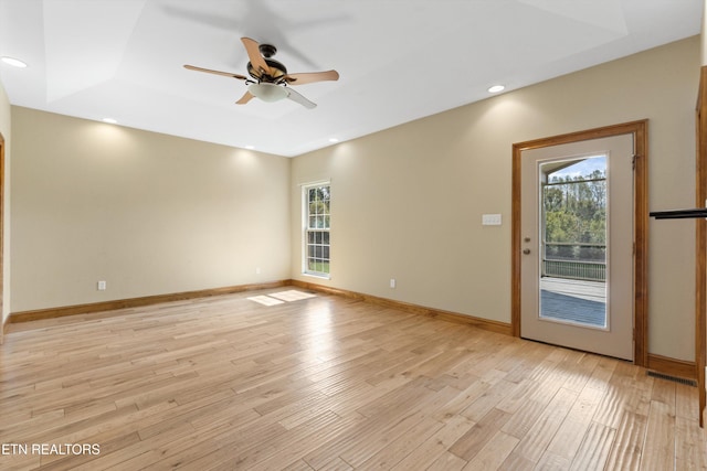 empty room with ceiling fan, light hardwood / wood-style flooring, a wealth of natural light, and a tray ceiling