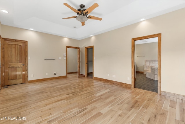 unfurnished bedroom featuring light wood-type flooring, a tray ceiling, ensuite bath, and ceiling fan