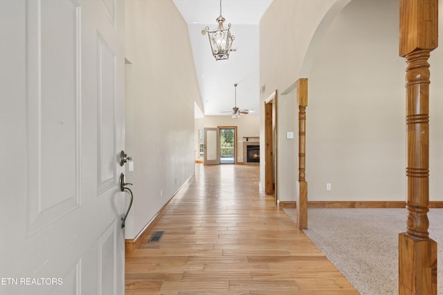 foyer entrance with a high ceiling, ceiling fan with notable chandelier, and light wood-type flooring