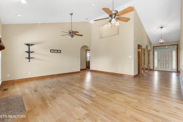 unfurnished living room with ceiling fan with notable chandelier, light wood-type flooring, and high vaulted ceiling