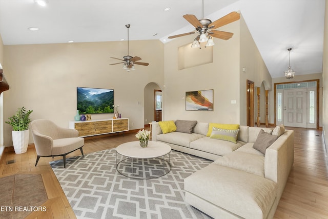 living room featuring hardwood / wood-style flooring, ceiling fan with notable chandelier, and high vaulted ceiling