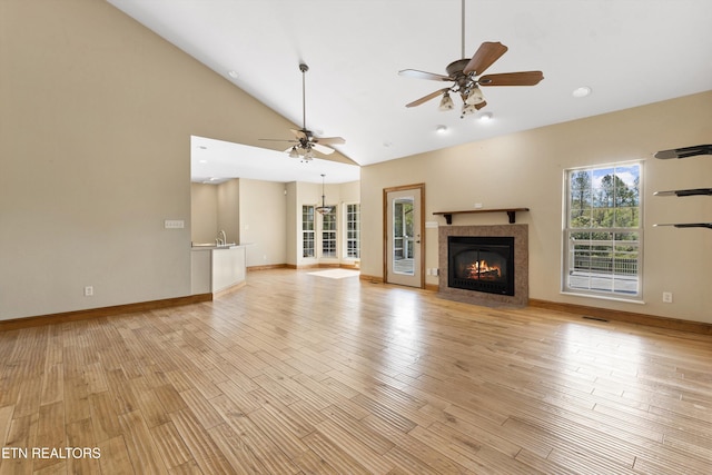 unfurnished living room featuring a fireplace, ceiling fan, light hardwood / wood-style flooring, and high vaulted ceiling