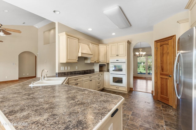 kitchen featuring custom range hood, ceiling fan with notable chandelier, double oven, sink, and stainless steel refrigerator