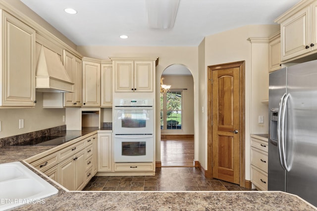 kitchen with cream cabinetry, stainless steel fridge, white double oven, and black electric cooktop