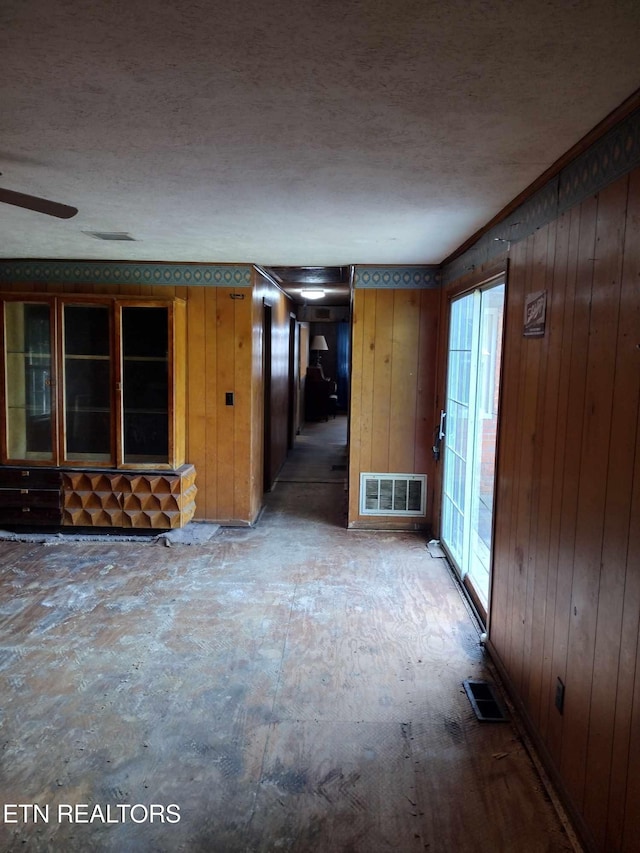 unfurnished room with a textured ceiling, ceiling fan, and wooden walls