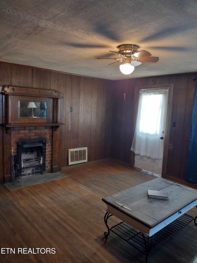 living room with a fireplace, wood walls, wood-type flooring, ceiling fan, and a textured ceiling