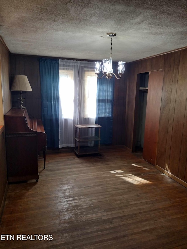 unfurnished dining area featuring an inviting chandelier, dark hardwood / wood-style floors, and wood walls