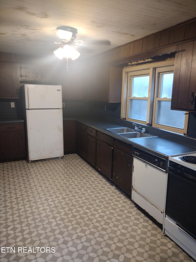 kitchen with white appliances, sink, dark brown cabinets, and wood walls