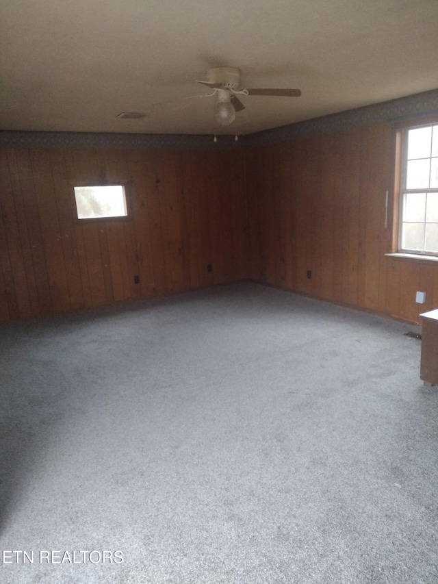 carpeted empty room with ceiling fan and wood walls