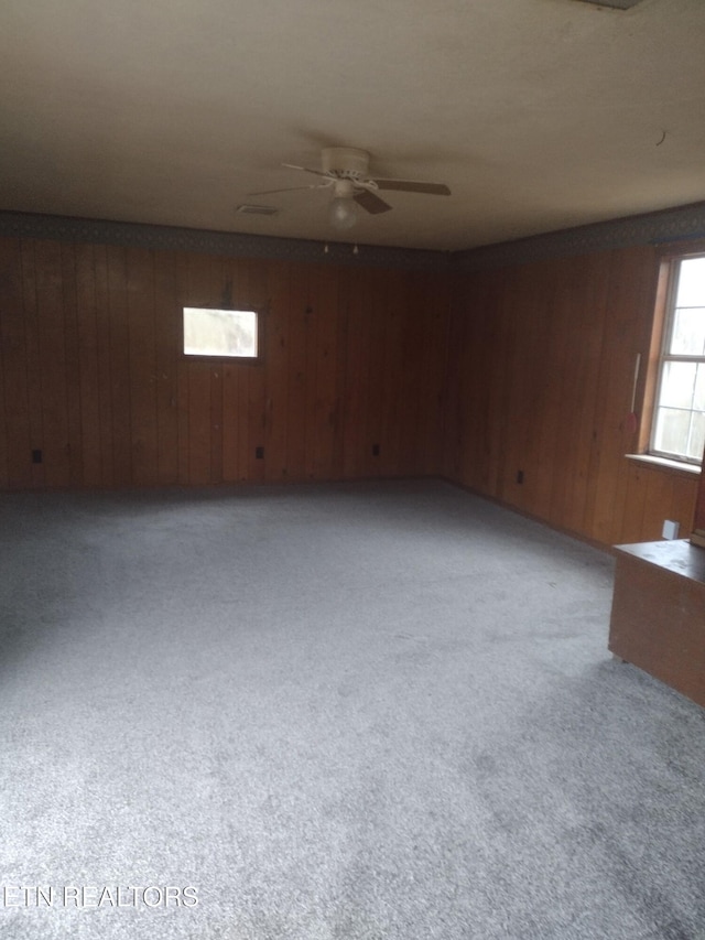 carpeted empty room featuring wooden walls and ceiling fan