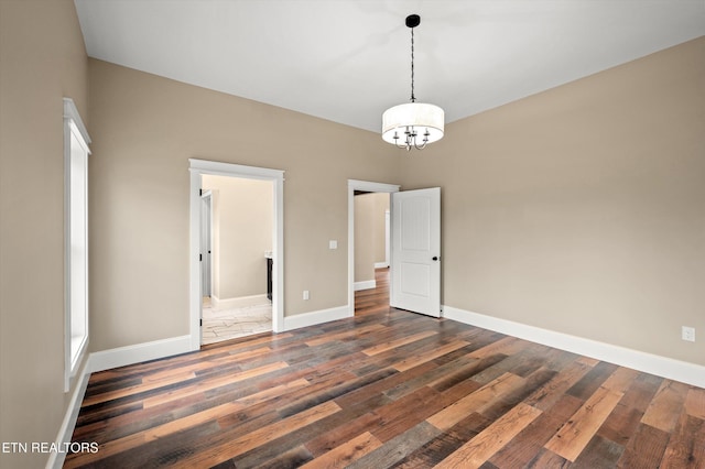 unfurnished room featuring baseboards, a notable chandelier, and dark wood-type flooring