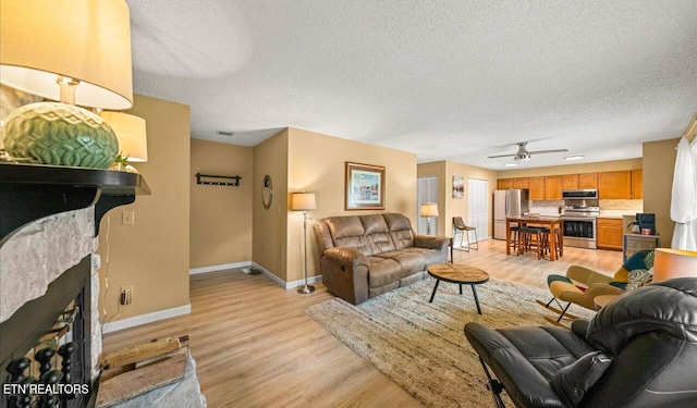 living room with a fireplace, ceiling fan, light hardwood / wood-style flooring, and a textured ceiling