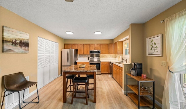 kitchen featuring backsplash, sink, light hardwood / wood-style flooring, a textured ceiling, and stainless steel appliances