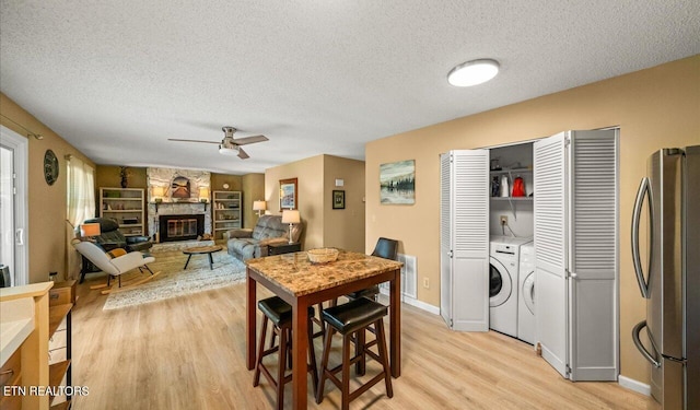 dining space featuring washer and clothes dryer, ceiling fan, light wood-type flooring, a fireplace, and a textured ceiling