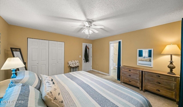 bedroom with ceiling fan, ensuite bathroom, light colored carpet, and a textured ceiling