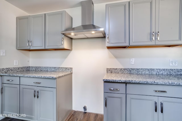 kitchen with dark hardwood / wood-style floors, light stone counters, gray cabinetry, and wall chimney range hood