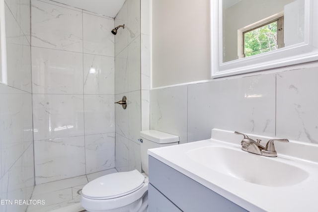 bathroom with a tile shower, vanity, toilet, and tile walls