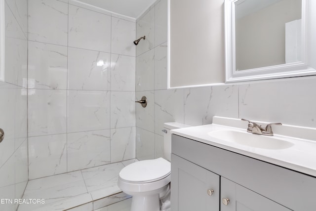 bathroom featuring vanity, toilet, a tile shower, and tile walls