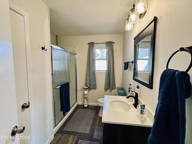 bathroom with vanity, a textured ceiling, hardwood / wood-style flooring, toilet, and a shower with shower door