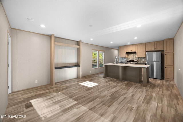 kitchen featuring stainless steel refrigerator, a breakfast bar, tasteful backsplash, a center island with sink, and light wood-type flooring