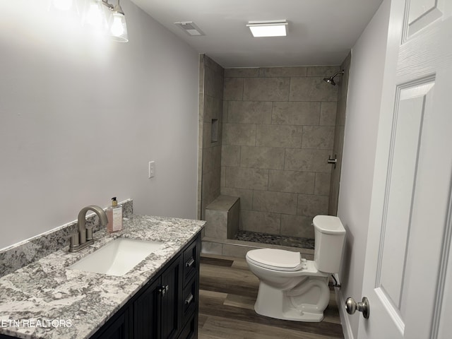 bathroom featuring tiled shower, hardwood / wood-style flooring, vanity, and toilet