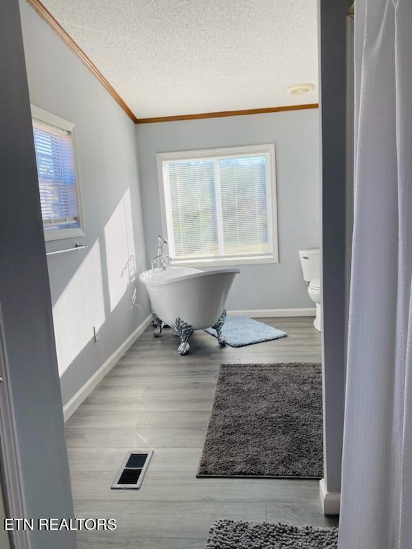 bathroom with a bathtub, toilet, ornamental molding, a textured ceiling, and wood-type flooring