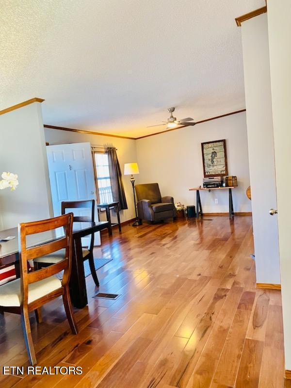 dining space with wood-type flooring, a textured ceiling, ceiling fan, and crown molding